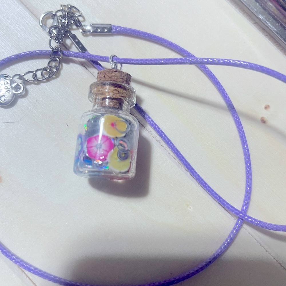 Cute bottle filled with flowers and silver glitter on a purple cord necklace
